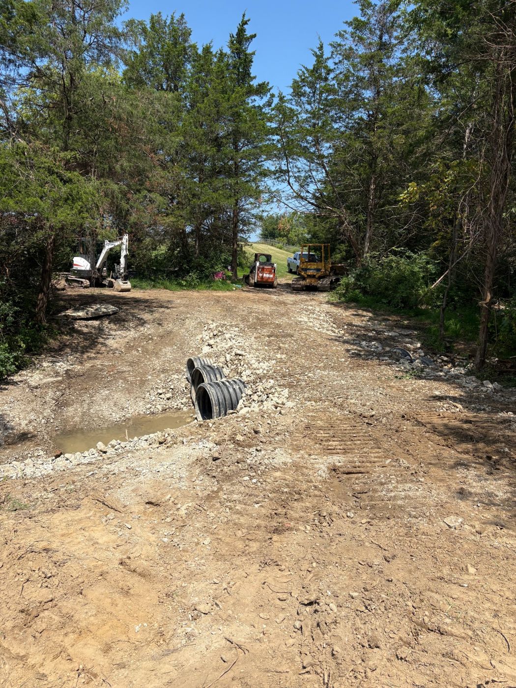 Culvert pipes set into a graded driveway entrance with a mini excavator, skid steer and dozer behind