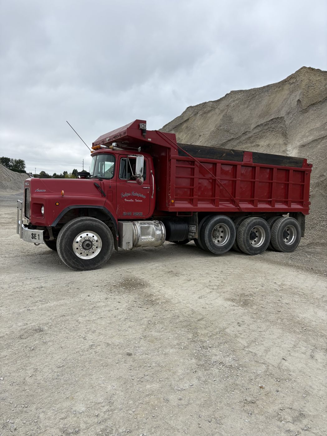 Red dump truck parked beside a large pile of stone